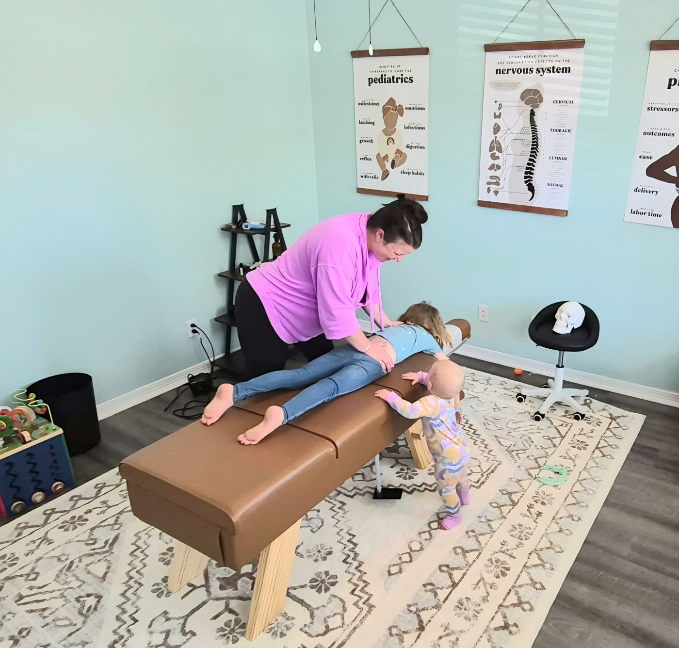 Dr. Kayla adjusting a young girl while a toddler watches