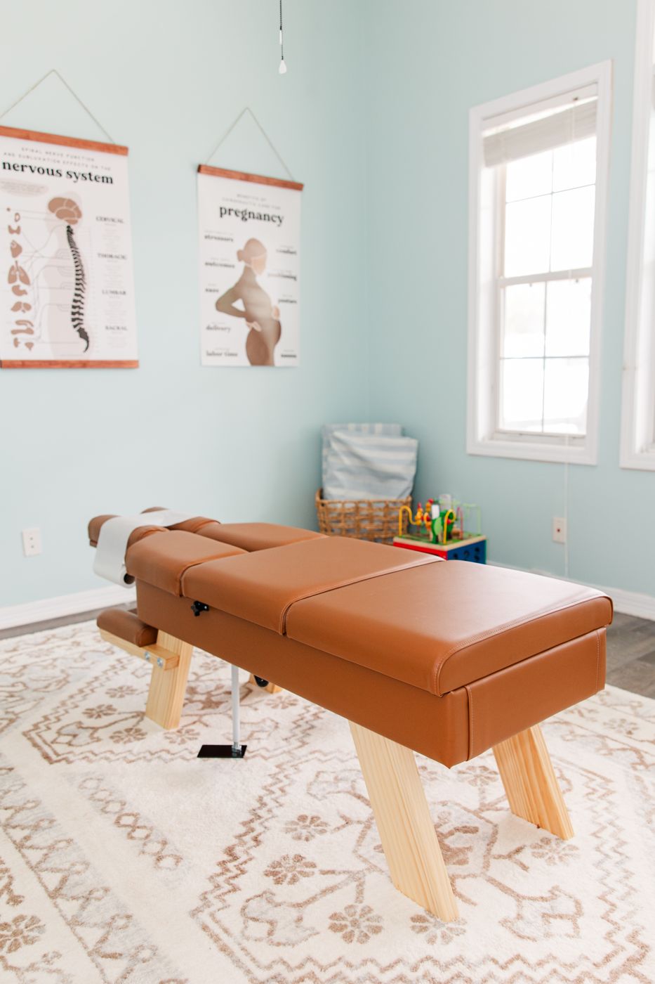 A bright adjusting room with a caramel table and pediatrics, nervous system, and pregnancy posters